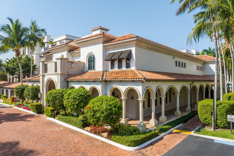 Building exterior with arched entry and palm trees at Heritage at Boca Raton